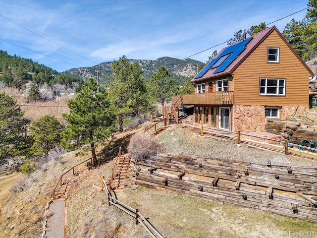 rear view of house with stone siding, solar panels, a deck with mountain view, and stairs