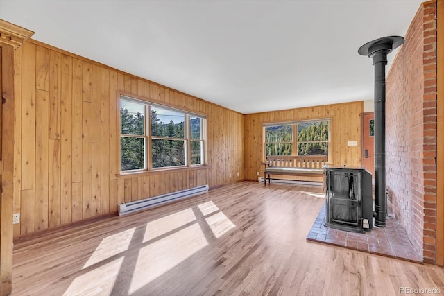 unfurnished living room with baseboard heating, wood walls, a wood stove, and wood finished floors