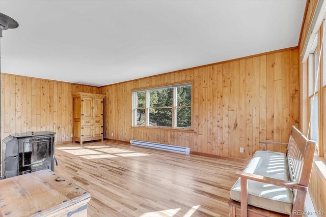 unfurnished living room featuring baseboards, light wood finished floors, a baseboard radiator, a wood stove, and wood walls