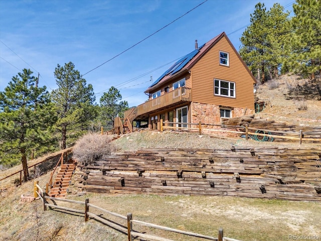 back of property featuring fence, stairway, metal roof, a deck, and stone siding