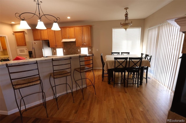 kitchen featuring stainless steel fridge with ice dispenser, decorative light fixtures, white microwave, and tasteful backsplash