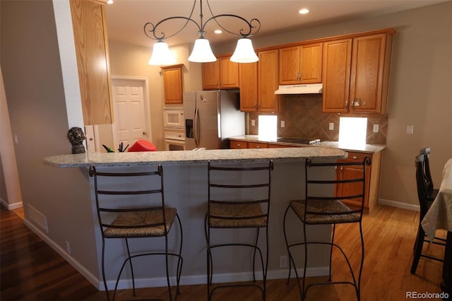 kitchen with kitchen peninsula, decorative light fixtures, light stone counters, white appliances, and decorative backsplash