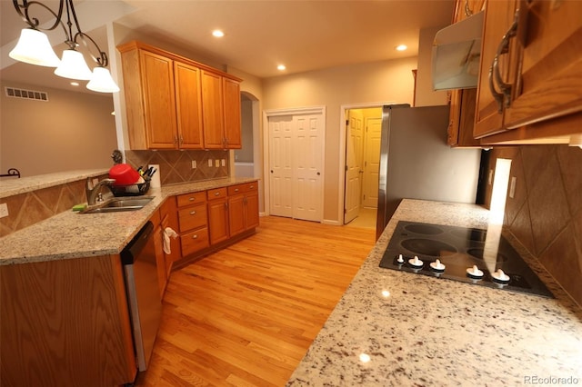 kitchen featuring black electric stovetop, stainless steel dishwasher, sink, decorative light fixtures, and light stone counters