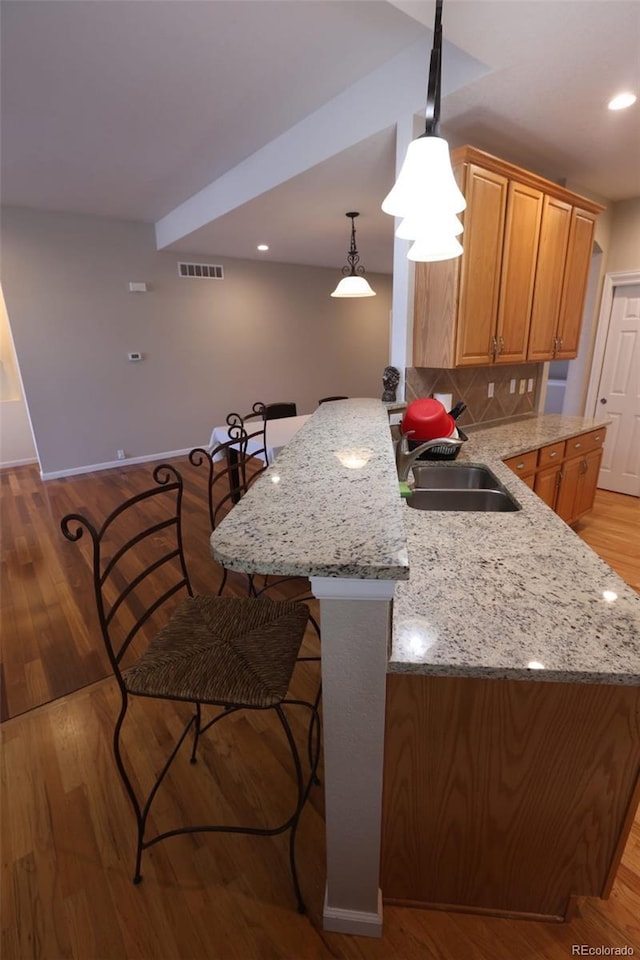 kitchen with light stone countertops, pendant lighting, sink, backsplash, and light hardwood / wood-style flooring