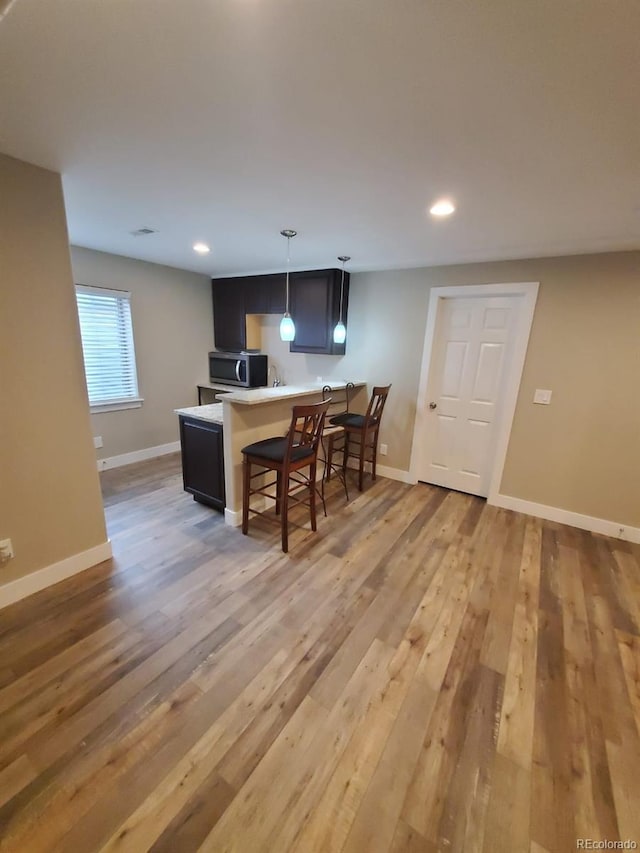 kitchen with a kitchen bar, decorative light fixtures, and light wood-type flooring