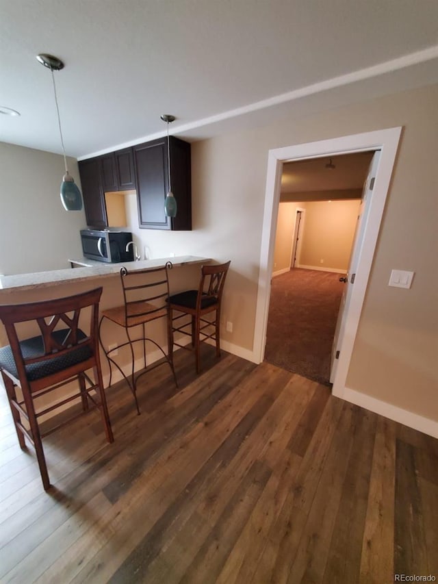 kitchen with a breakfast bar area, decorative light fixtures, kitchen peninsula, and dark hardwood / wood-style floors