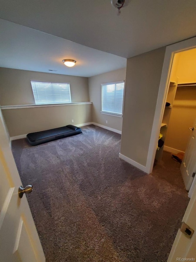 interior space with dark colored carpet, a closet, and a walk in closet