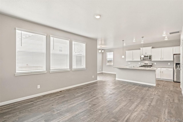 kitchen featuring stainless steel appliances, light hardwood / wood-style flooring, white cabinets, hanging light fixtures, and an island with sink