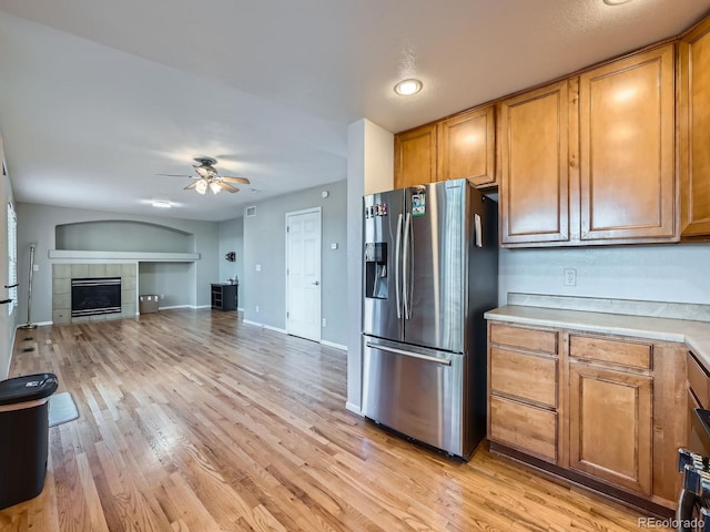 kitchen featuring ceiling fan, stainless steel refrigerator with ice dispenser, a tile fireplace, and light hardwood / wood-style flooring