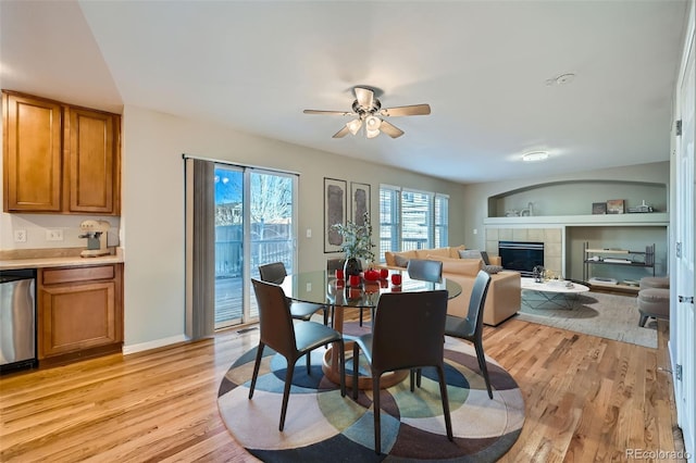 dining area with a tiled fireplace, ceiling fan, and light hardwood / wood-style flooring