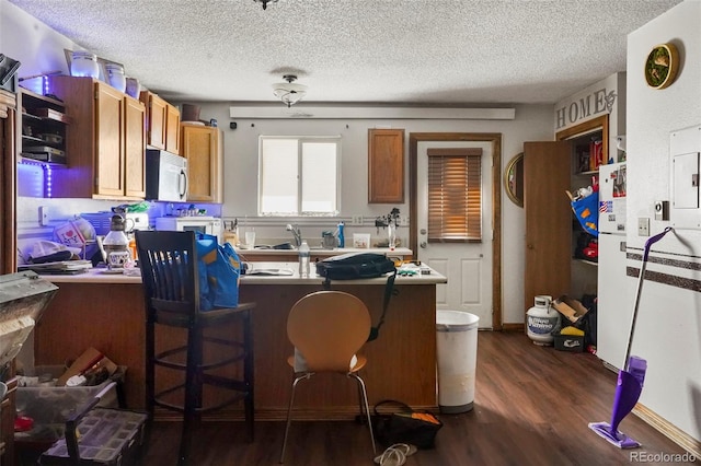 2480 Allegheny Dr, Colorado Springs, CO 80919 - kitchen featuring white microwave, a peninsula, dark wood-style flooring, a textured ceiling, and brown cabinetry