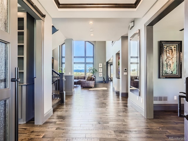 corridor with dark wood-type flooring, ornamental molding, and a barn door