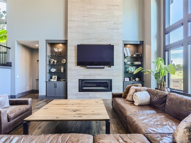 living room featuring a tiled fireplace, a towering ceiling, hardwood / wood-style floors, and built in features