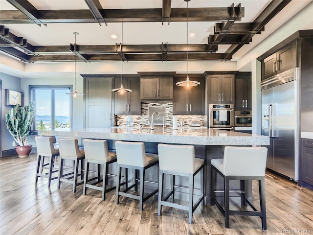 kitchen with built in refrigerator, a spacious island, dark brown cabinets, and decorative light fixtures