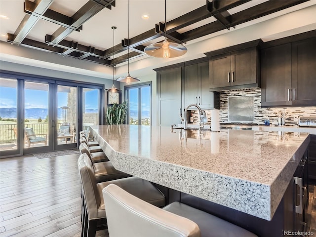 kitchen featuring coffered ceiling, hanging light fixtures, dark hardwood / wood-style flooring, an island with sink, and backsplash