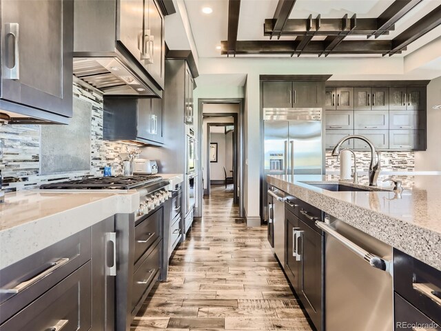 kitchen with backsplash, stainless steel appliances, light stone countertops, and light wood-type flooring