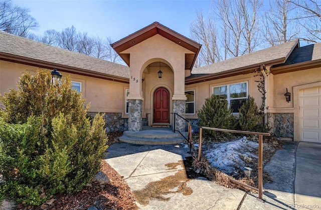 doorway to property with a garage, stone siding, and stucco siding