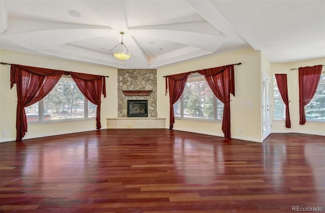 unfurnished living room featuring a tray ceiling, a fireplace, wood finished floors, and baseboards