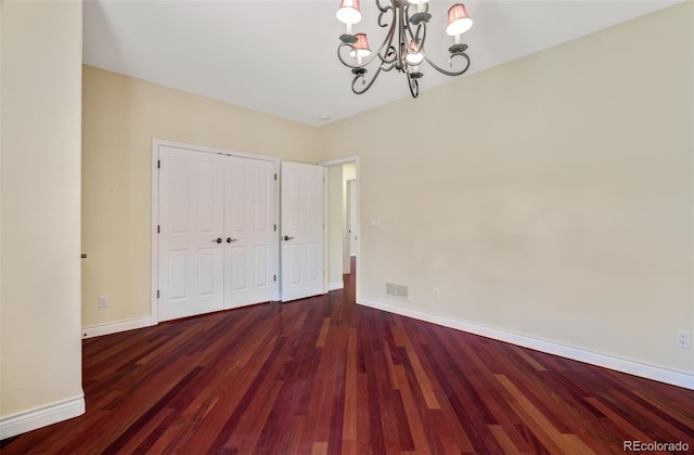 unfurnished bedroom with baseboards, visible vents, wood finished floors, an inviting chandelier, and a closet