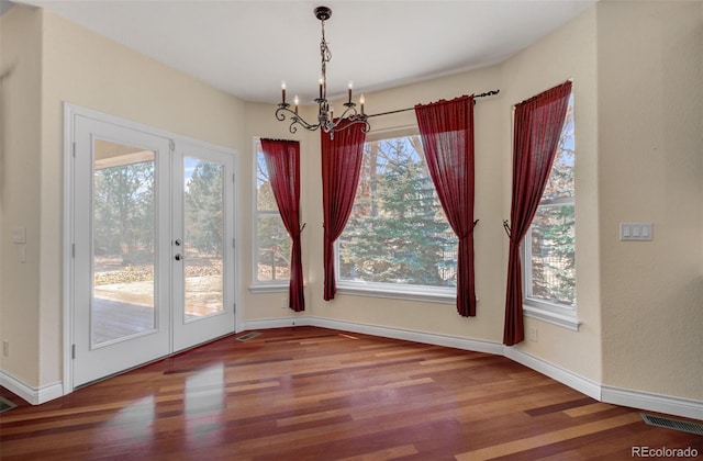 unfurnished dining area featuring baseboards, wood finished floors, visible vents, and an inviting chandelier