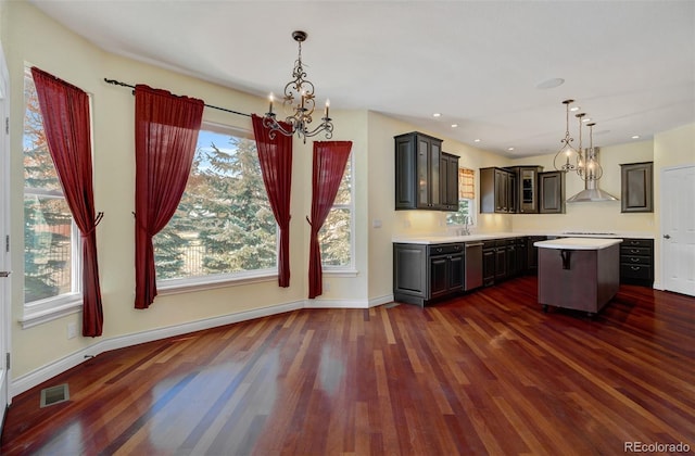 kitchen featuring a chandelier, dark wood-type flooring, light countertops, a center island, and wall chimney exhaust hood