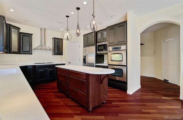 kitchen featuring stainless steel appliances, light countertops, wall chimney range hood, a center island, and dark wood finished floors