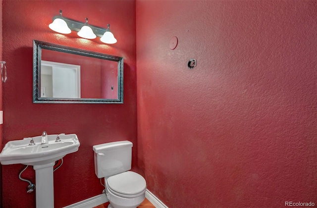 half bath with toilet, baseboards, and a sink