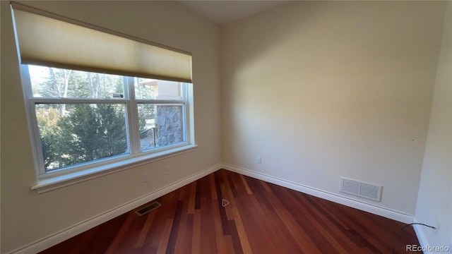 empty room with dark wood finished floors, visible vents, and baseboards