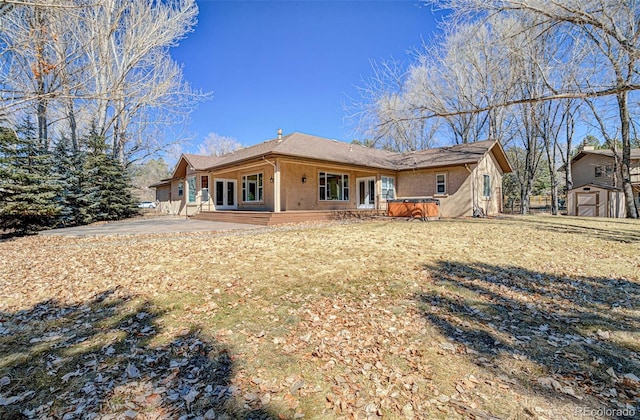 rear view of house with an outbuilding, french doors, stucco siding, a hot tub, and a shed