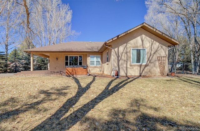 rear view of property with a hot tub, fence, a lawn, and stucco siding