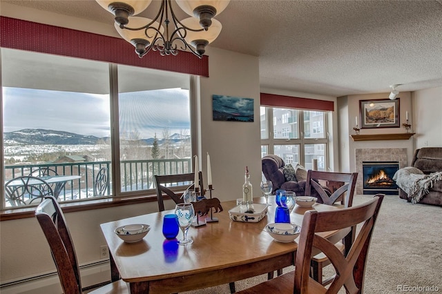 carpeted dining space featuring a textured ceiling, baseboard heating, a mountain view, a notable chandelier, and a tiled fireplace