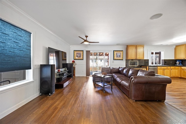 living area featuring crown molding, baseboards, ceiling fan, and dark wood-type flooring