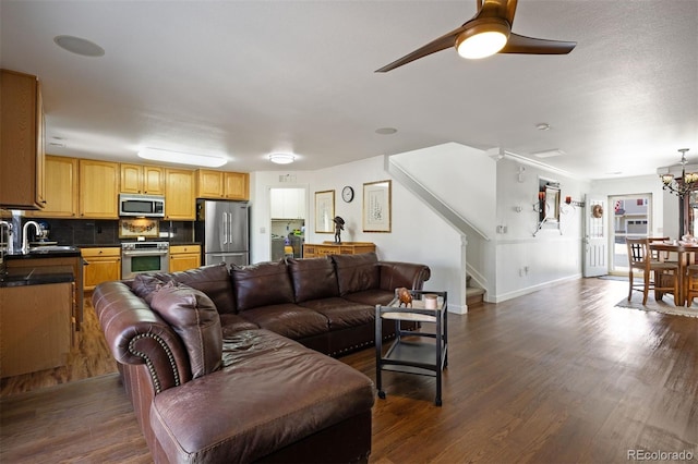 living area featuring stairway, baseboards, ceiling fan with notable chandelier, and dark wood finished floors