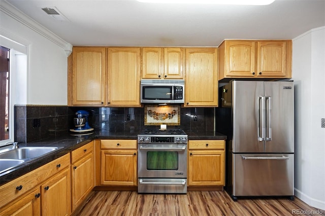 kitchen featuring visible vents, wood finished floors, a sink, backsplash, and stainless steel appliances