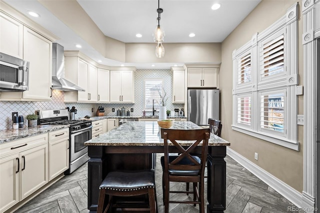 kitchen featuring appliances with stainless steel finishes, wall chimney exhaust hood, a kitchen breakfast bar, decorative backsplash, and a kitchen island