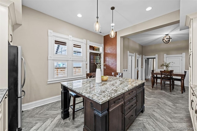 kitchen with freestanding refrigerator, recessed lighting, baseboards, a kitchen island, and dark brown cabinets