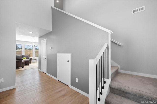 stairway with visible vents, baseboards, a high ceiling, an inviting chandelier, and wood finished floors