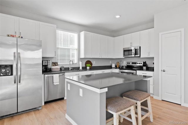 kitchen featuring a breakfast bar area, a sink, stainless steel appliances, white cabinets, and dark countertops