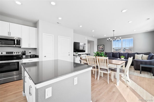 kitchen with open floor plan, stainless steel appliances, white cabinets, light wood finished floors, and a chandelier