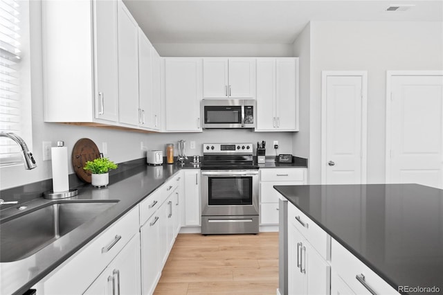 kitchen with dark countertops, light wood-type flooring, stainless steel appliances, white cabinetry, and a sink