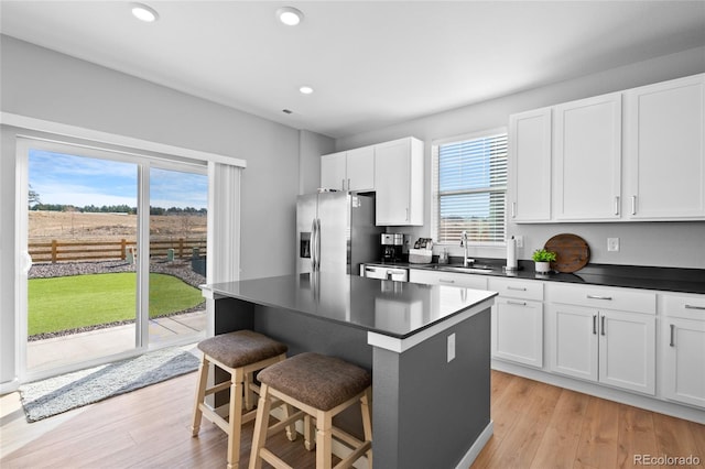 kitchen with dark countertops, light wood finished floors, a breakfast bar, stainless steel appliances, and a sink