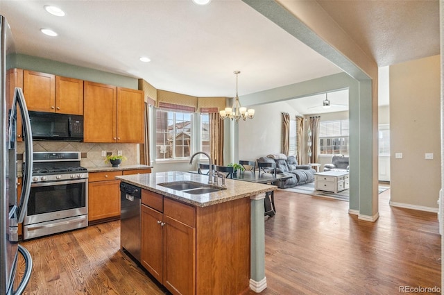 kitchen with light stone counters, stainless steel appliances, wood finished floors, a sink, and plenty of natural light