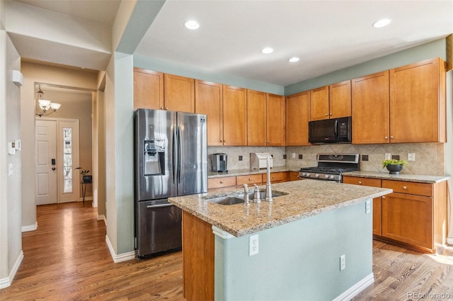 kitchen featuring decorative backsplash, light stone counters, stainless steel appliances, light wood-type flooring, and a sink