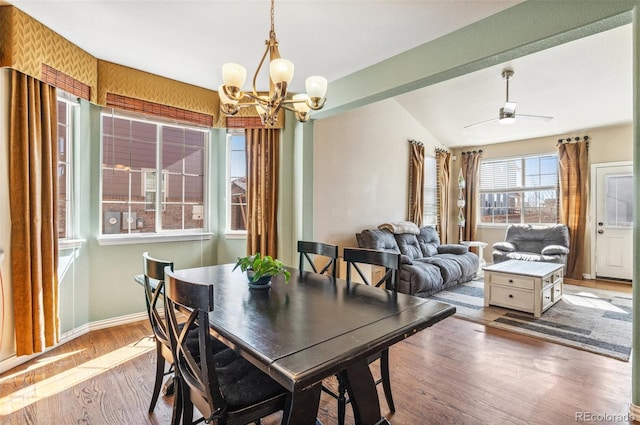 dining area with ceiling fan with notable chandelier, vaulted ceiling, wood finished floors, and baseboards