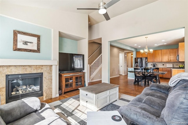 living room featuring a tile fireplace, light wood-style flooring, ceiling fan with notable chandelier, stairs, and vaulted ceiling