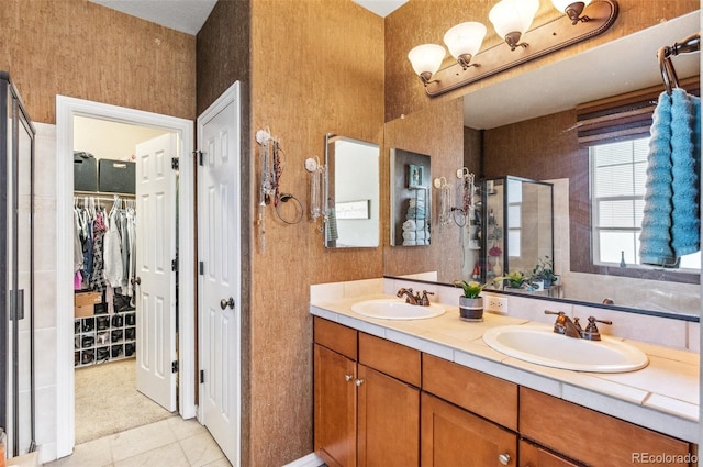 full bathroom featuring double vanity, a sink, a walk in closet, and a shower stall