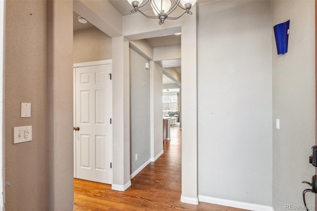 hall featuring baseboards, wood finished floors, and an inviting chandelier