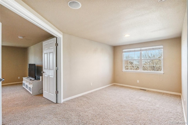 unfurnished room with a textured ceiling, carpet flooring, visible vents, and baseboards