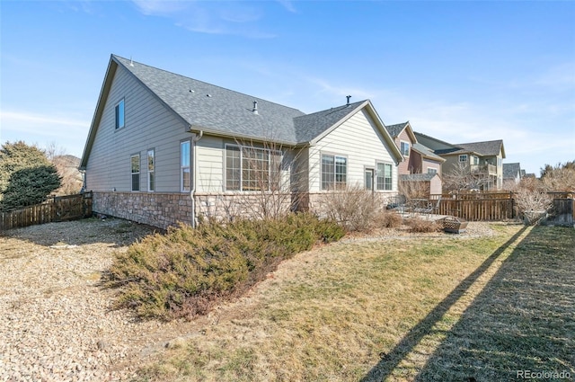 back of property with stone siding, a shingled roof, fence, and a yard