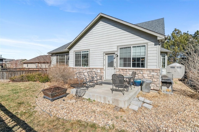 rear view of house featuring a shingled roof, a fire pit, a patio, stone siding, and fence